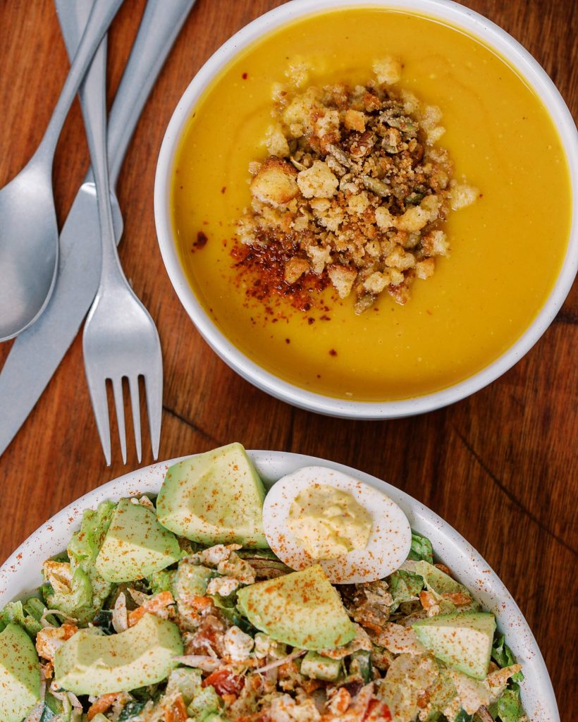 A bowl of creamy yellow soup topped with croutons and a salad with avocado, eggs, and dressing in Williamson County, Tennessee.