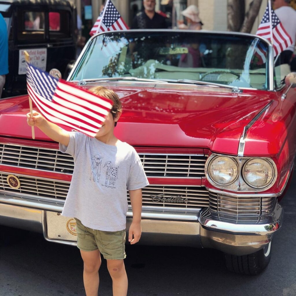 A young boy proudly waves an American flag in front of a classic red convertible Cadillac in Williamson County, Tennessee.