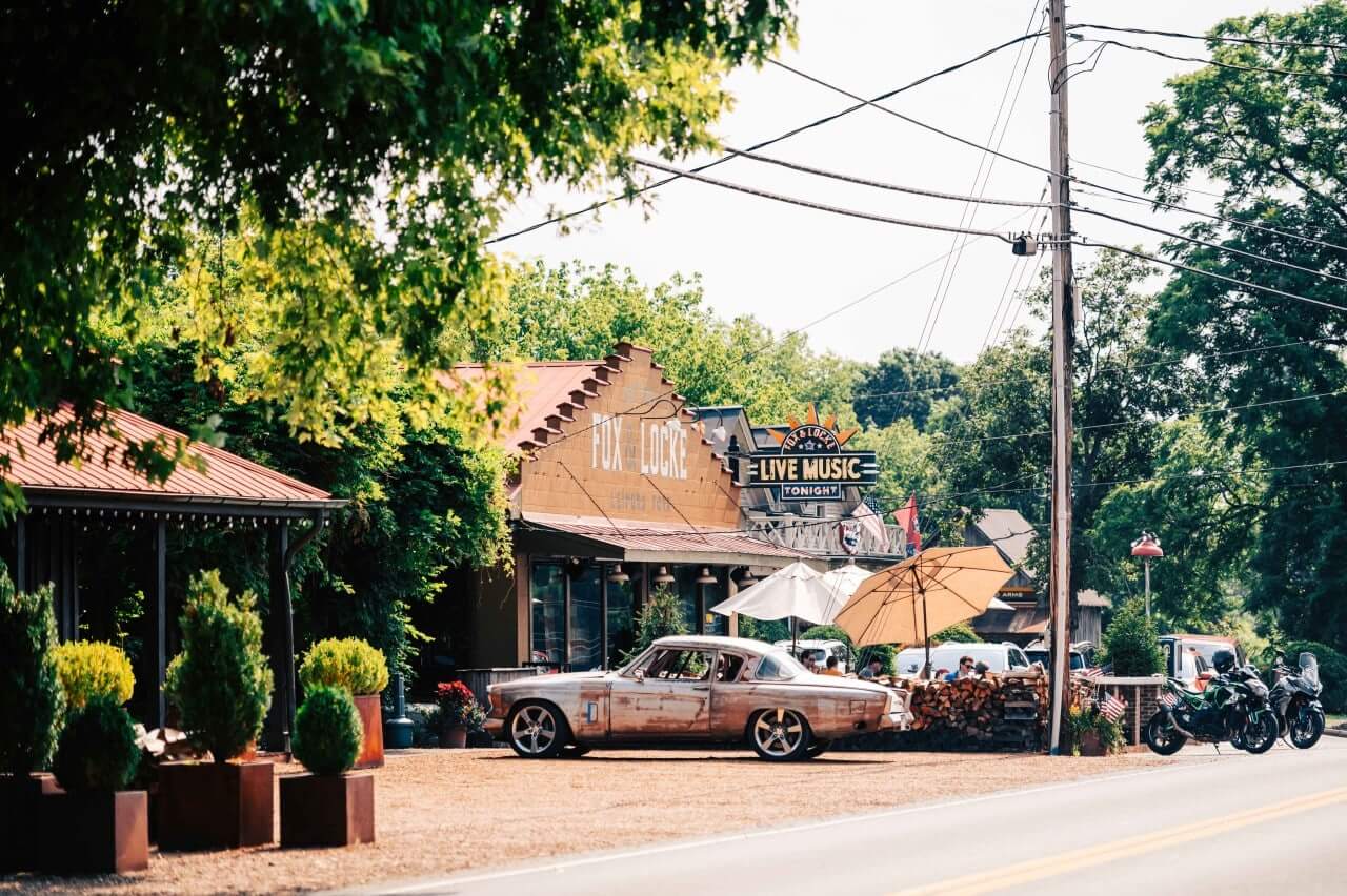 12 Amazing Things to Do in Charming Leiper's Fork, Tennessee A vintage car is parked outside a live music venue with outdoor seating and umbrellas in Williamson County, Tennessee.