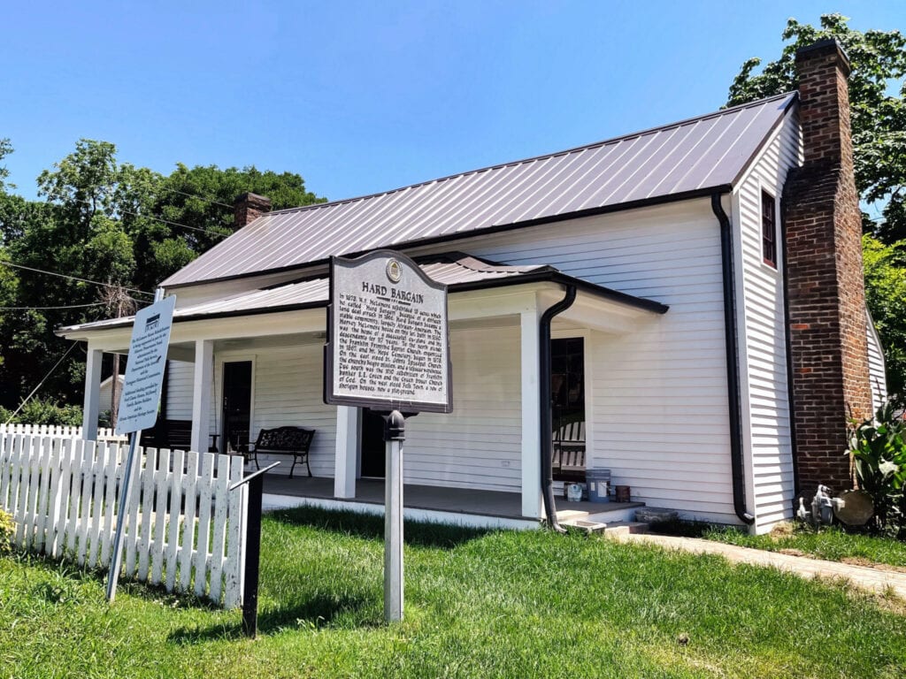White house with metal roof, brick chimney, and porch, surrounded by green lawn and white picket fence in Williamson County, Tennessee.