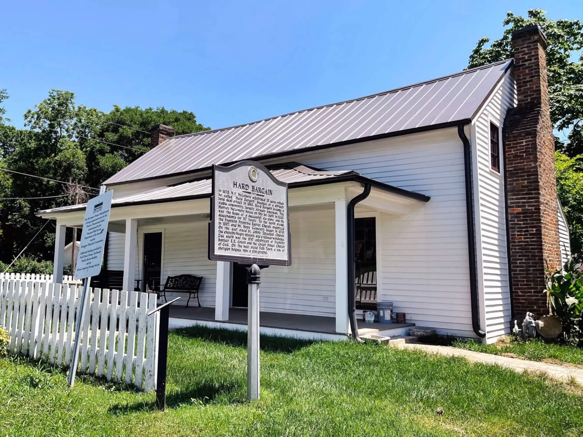 Discover the Fascinating History of Franklin's Black Citizens on This House Tour White house with metal roof, brick chimney, and porch, surrounded by green lawn and white picket fence in Williamson County, Tennessee.