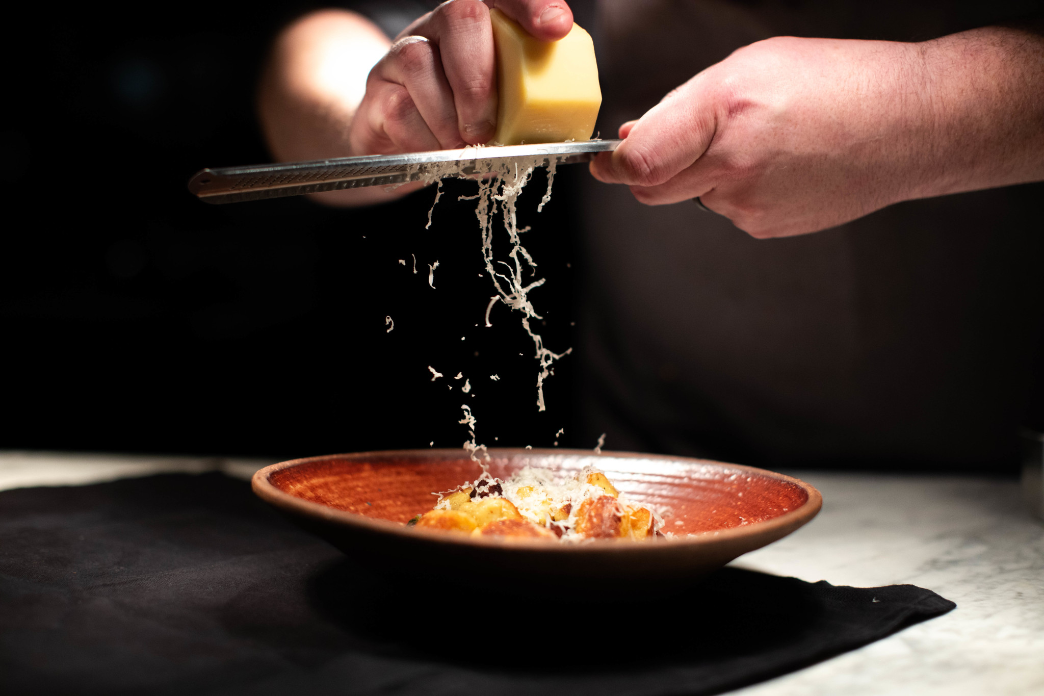 How Local Farms & Artisans Are Inspiring Franklin Chefs' World-Class Menus A chef's hands grate Parmesan cheese over a dish of pasta in a rustic bowl in Williamson County, Tennessee.