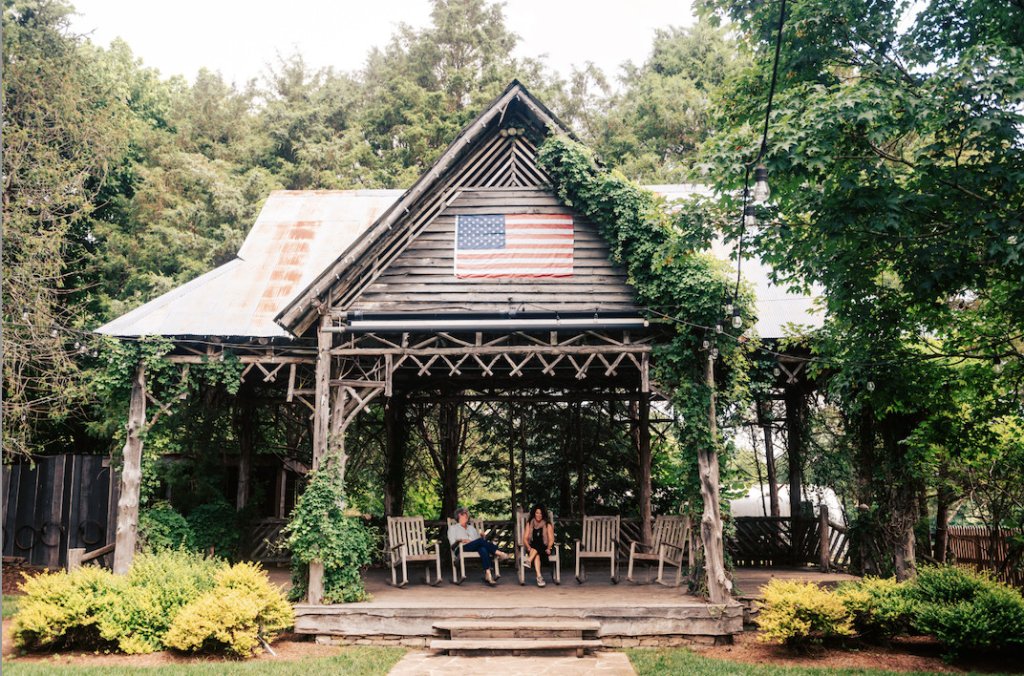 How to Make the Most of a Day Trip to Leiper's Fork Rustic wooden gazebo with American flag, surrounded by lush greenery and two people sitting inside in Williamson County, Tennessee.