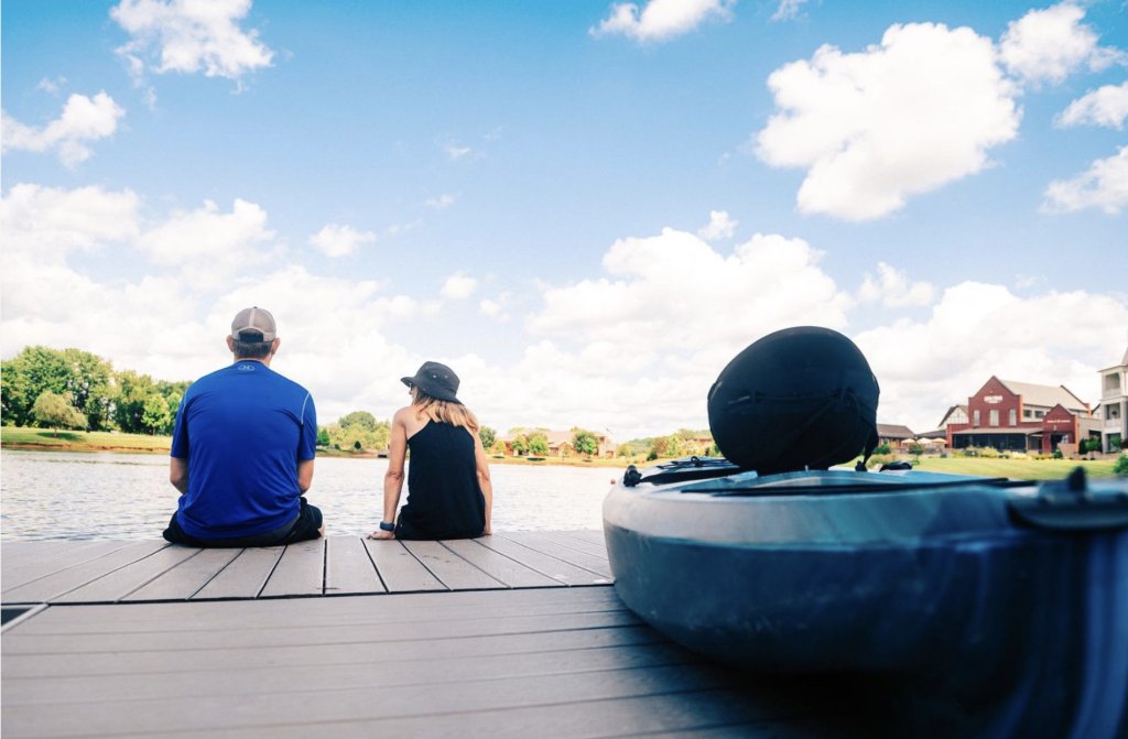 Perfect Picnic Pairings for a Lovely Day in Franklin A couple sits on a wooden dock overlooking a serene lake with a kayak nearby in Williamson County, Tennessee.