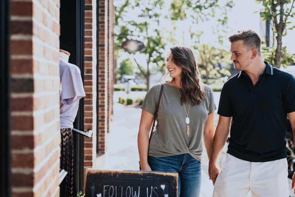 A couple walks past a brick building with a sign reading 'Follow Us' and clothing displayed in the window in Williamson County, Tennessee.