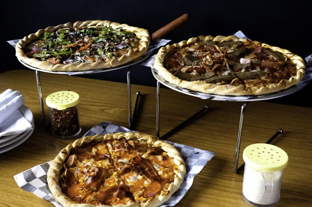 Three different pizzas displayed on stands with toppings including vegetables, meats, and cheese in Williamson County, Tennessee.