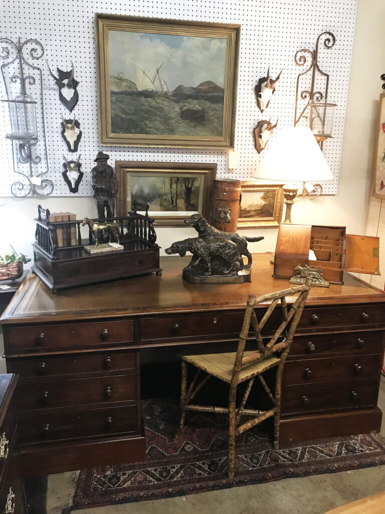 A vintage wooden desk with a chair, lamp, and various decorative items including paintings and sculptures in Williamson County, Tennessee.