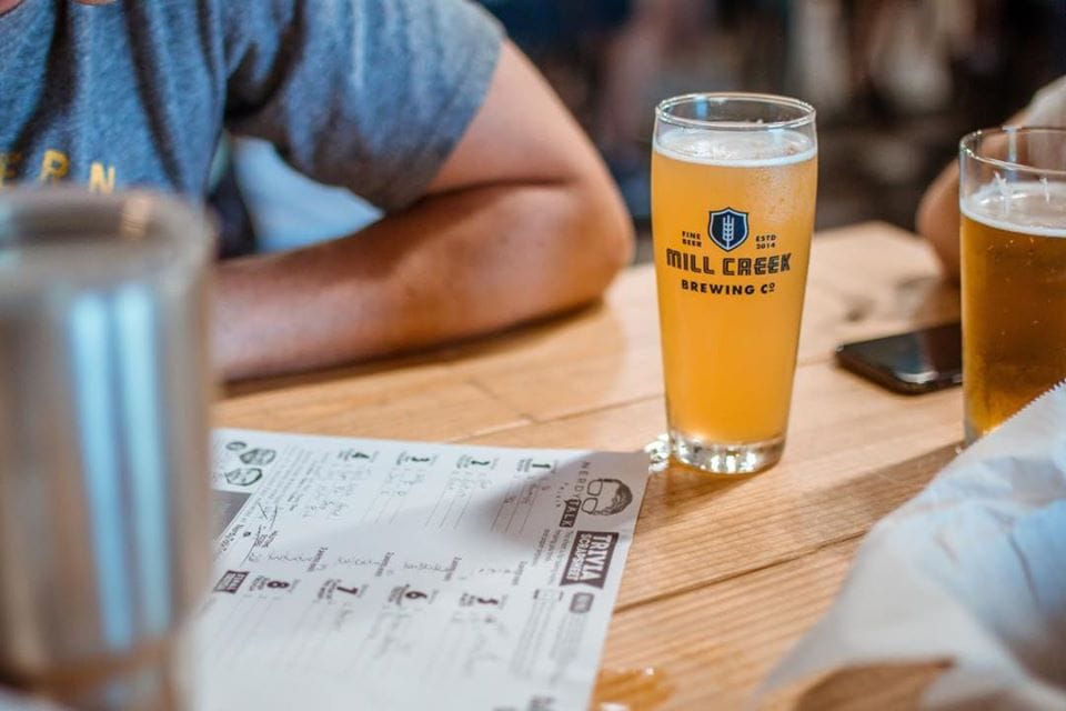 A person sits at a wooden table with two glasses of beer and a menu in Williamson County, Tennessee.