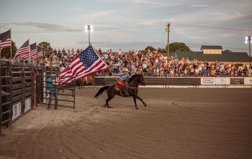 Events A cowboy gallops around a rodeo arena, waving an American flag, as a large crowd cheers from the stands in Williamson County, Tennessee.