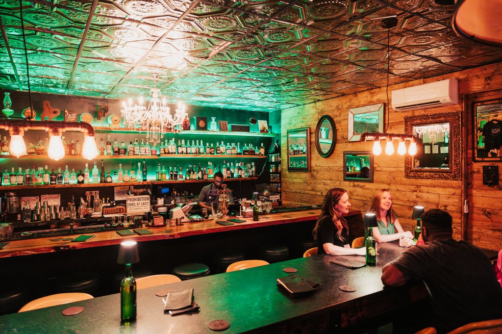 A dimly lit bar with a green-tiled ceiling, wooden walls, and a long counter filled with bottles and patrons in Williamson County, Tennessee.