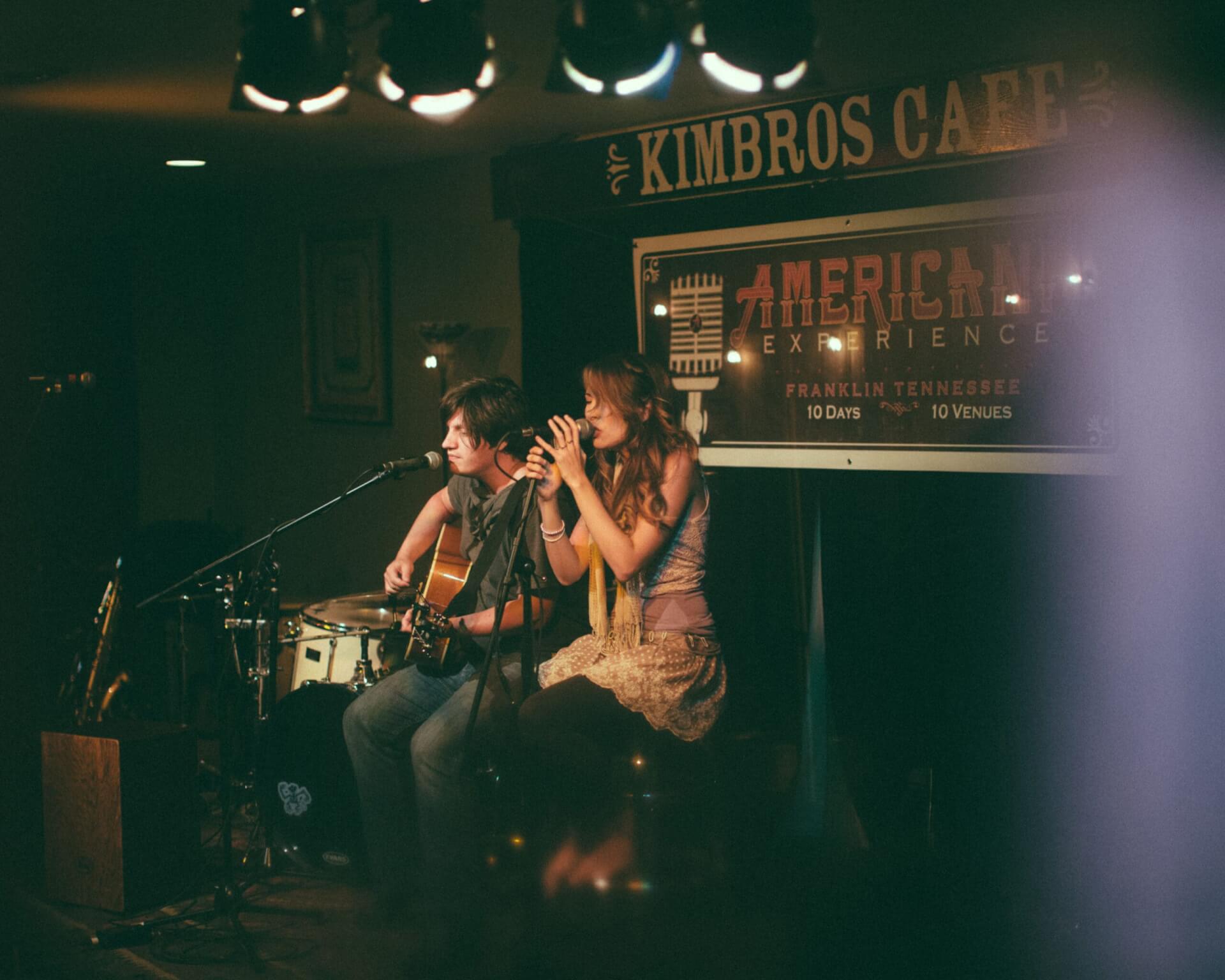 Two musicians perform at Kimbros Cafe, one playing guitar and the other singing into a microphone in Williamson County, Tennessee.