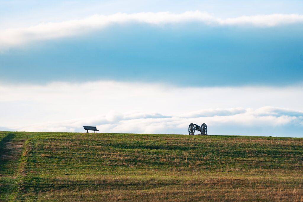 A lone bench overlooks a vast grassy field with a cannon in the distance in Williamson County, Tennessee.