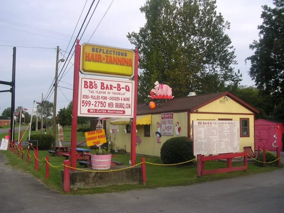 A quaint yellow BBQ restaurant with red accents and outdoor seating, featuring a large pig statue on the roof in Williamson County, Tennessee.