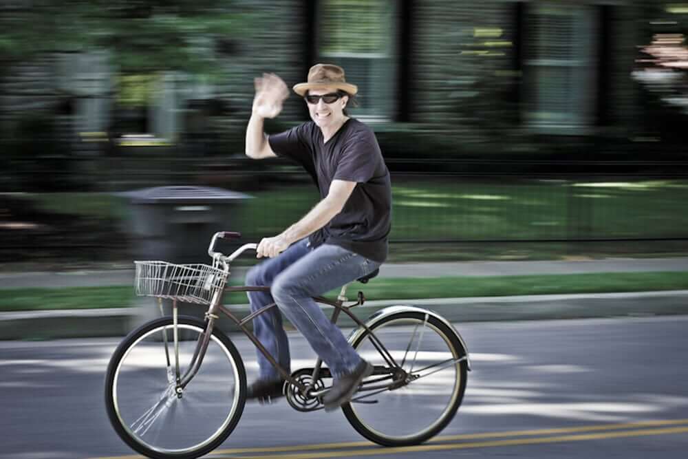 Your Guide To The Best Biking In Williamson County A man wearing a hat and sunglasses waves while riding a bicycle with a basket in Williamson County, Tennessee.