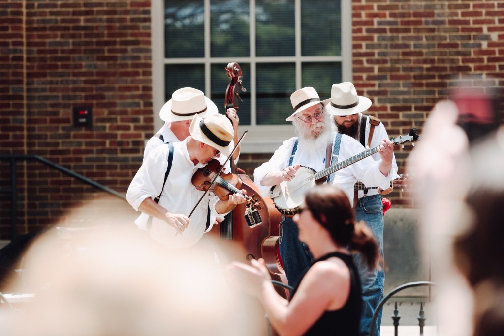 Let's Get Festive! Here Are the Essential Summer Events in Franklin, Tennessee A lively string band performs outdoors, with five musicians dressed in white shirts, suspenders, and hats, playing violin, cello, banjo, and guitar in front of a brick building in Williamson County, Tennessee.