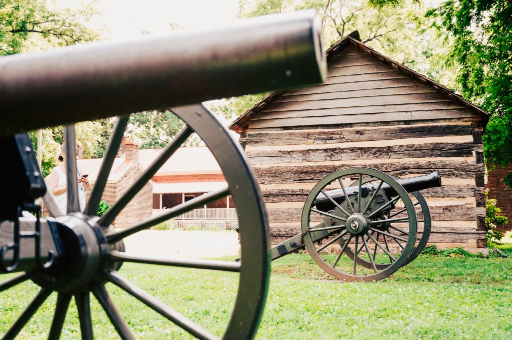 Franklin, Tennessee's Preservation Success Story A cannon points towards a rustic log cabin surrounded by lush green grass and trees in Williamson County, Tennessee.