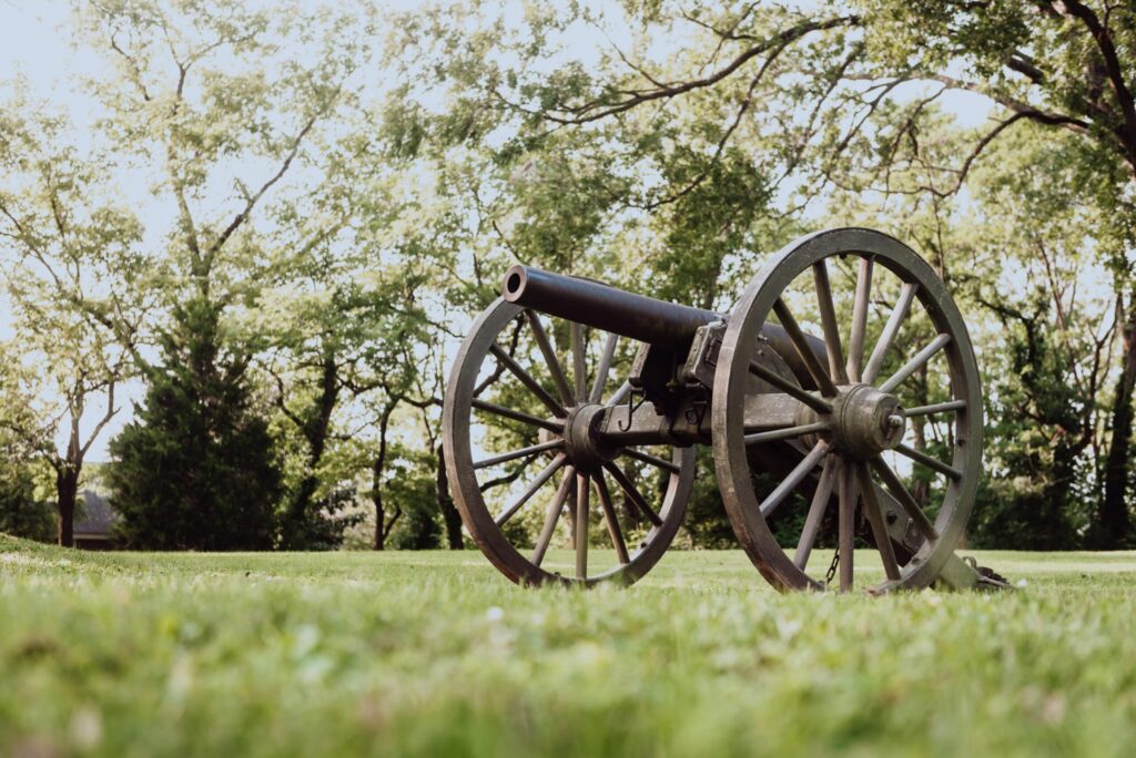 An old cannon with wooden wheels rests on a grassy field, surrounded by trees in Williamson County, Tennessee.