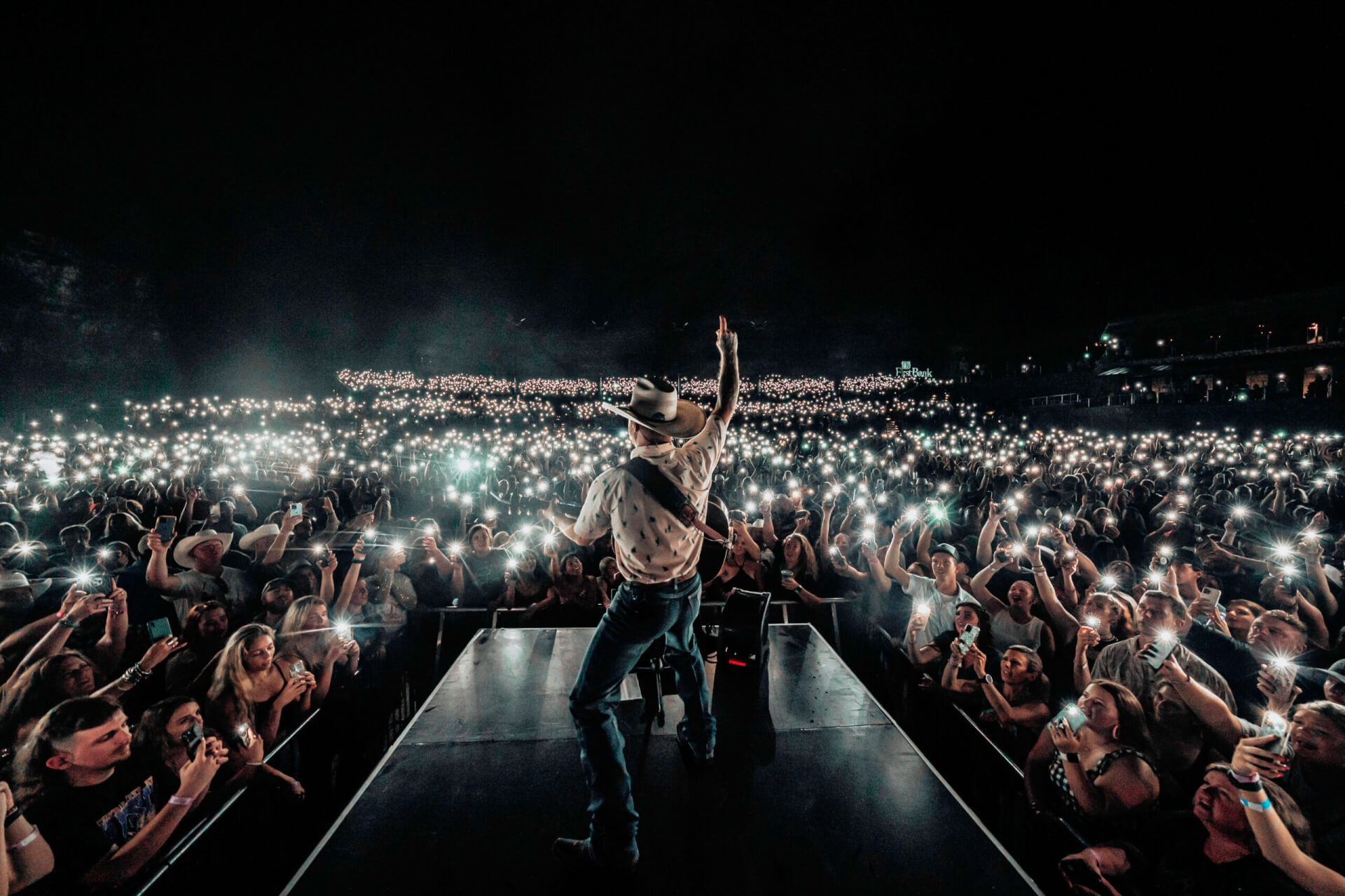 A musician performs on stage, bathed in light, as a sea of glowing phones fills the arena in Williamson County, Tennessee.