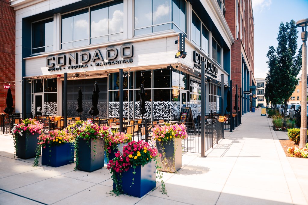 Celebrate Patio Season at Some of Franklin's Best Outdoor Dining Experiences A vibrant outdoor seating area at Condado restaurant, adorned with colorful flower pots and black umbrellas, inviting patrons to enjoy tacos, tequila, and margaritas in Williamson County, Tennessee.