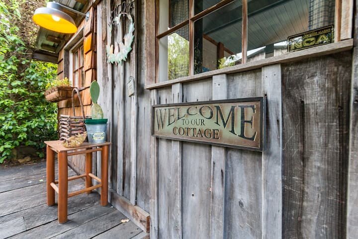 A rustic wooden cottage with a 'Welcome to Our Cottage' sign and a small table with plants in Williamson County, Tennessee.