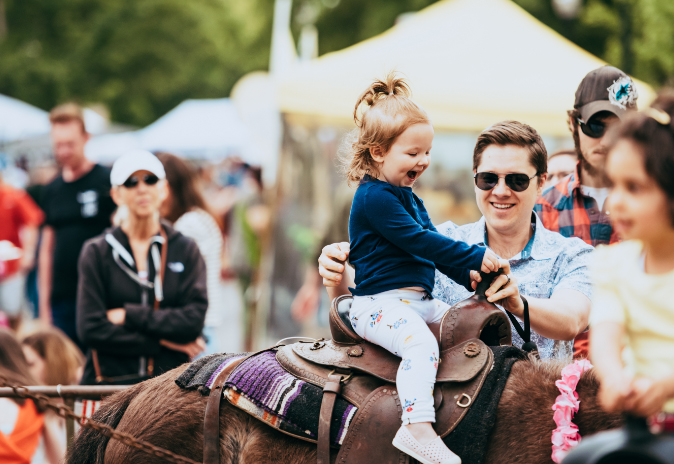 Communities A young girl joyfully rides a pony at a fair, accompanied by her smiling father in Williamson County, Tennessee.
