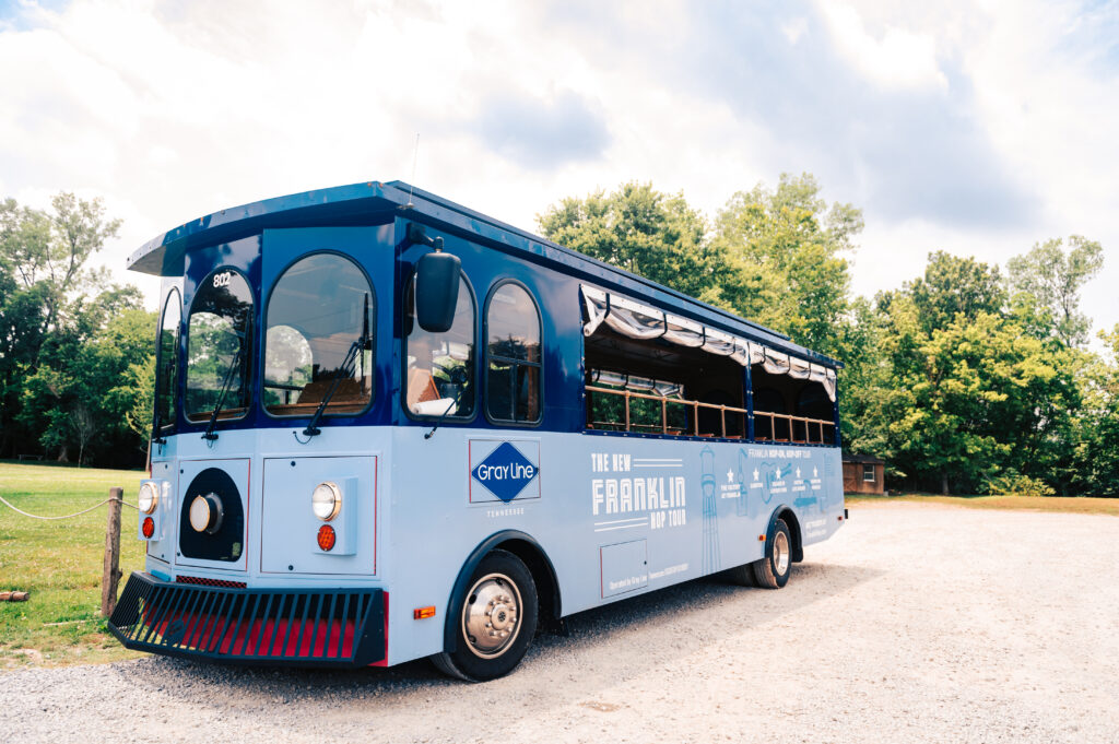 A blue and white trolley bus with 'Franklin' branding is parked on gravel near trees in Williamson County, Tennessee.