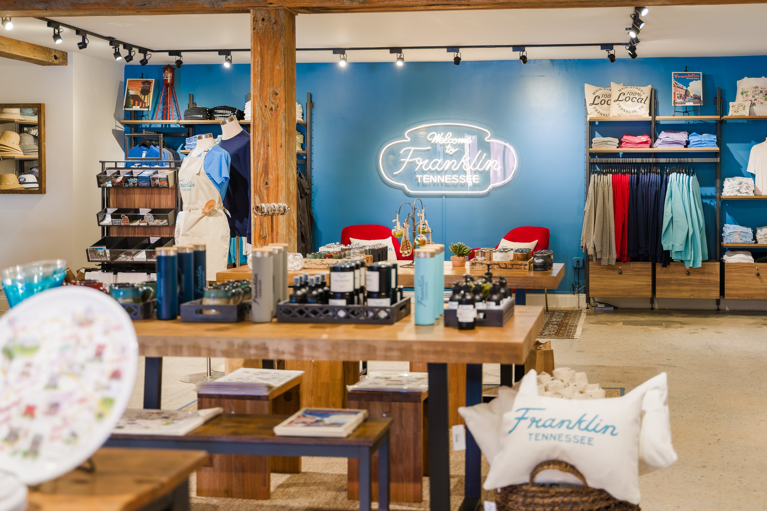 A brightly lit boutique with clothing racks, wooden tables, and a neon sign reading 'Welcome to Franklin, Tennessee' in Williamson County, Tennessee.