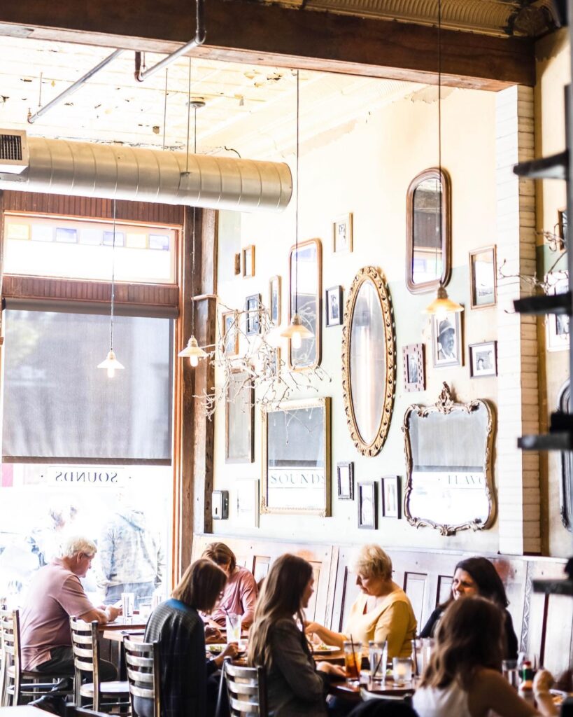 A cozy restaurant interior with a rustic wooden ceiling, framed mirrors, and patrons dining at tables in Williamson County, Tennessee.