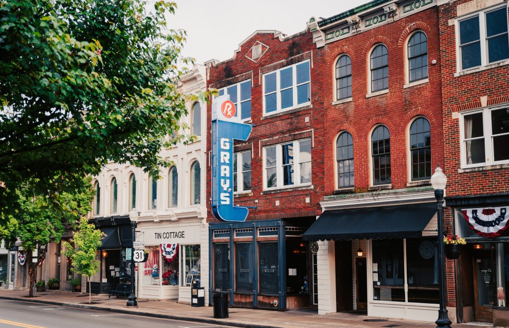 Franklin, Tennessee's Preservation Success Story A charming downtown street lined with historic brick buildings, featuring a prominent blue neon sign for Gray's Drug Store and other quaint shops with awnings in Williamson County, Tennessee.