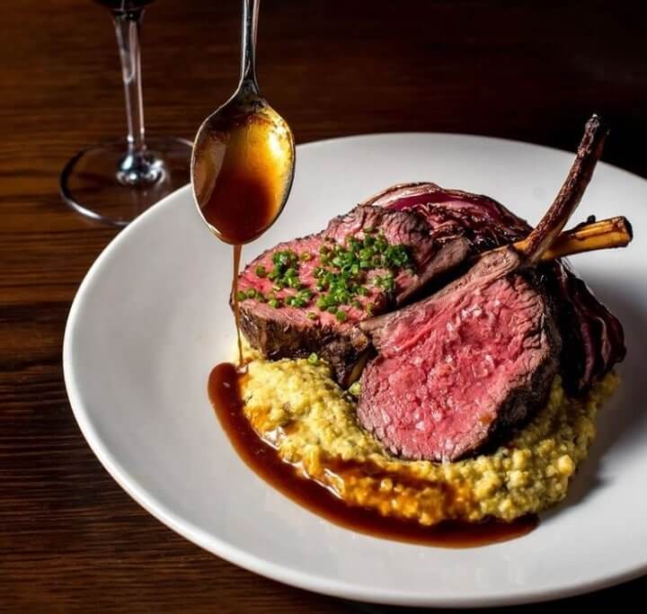 A plate of medium-rare lamb chops with a creamy base and a spoonful of rich gravy in Williamson County, Tennessee.