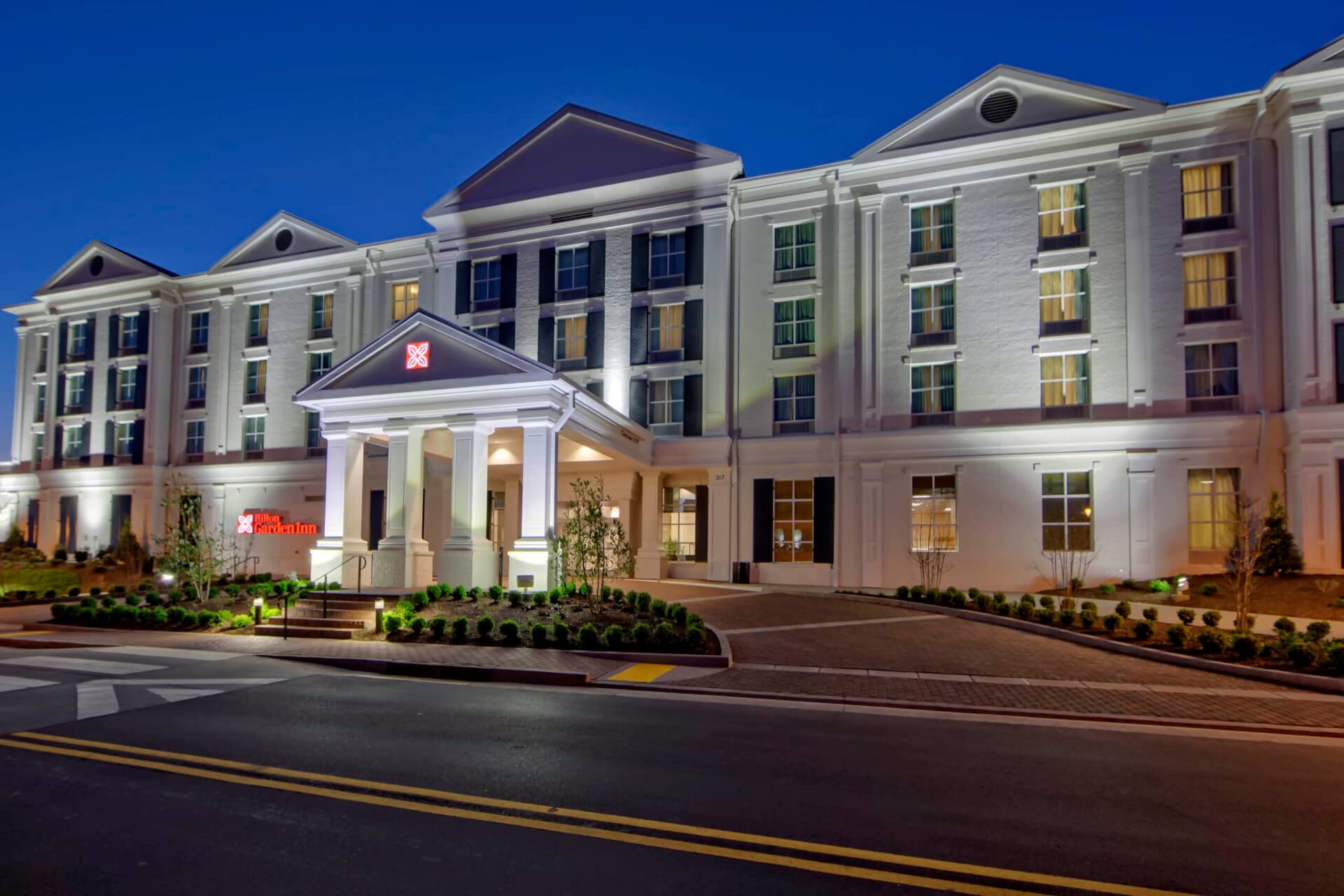 Hilton Garden Inn Nashville Brentwood A large, white hotel with columns and a red sign, illuminated at night in Williamson County, Tennessee.