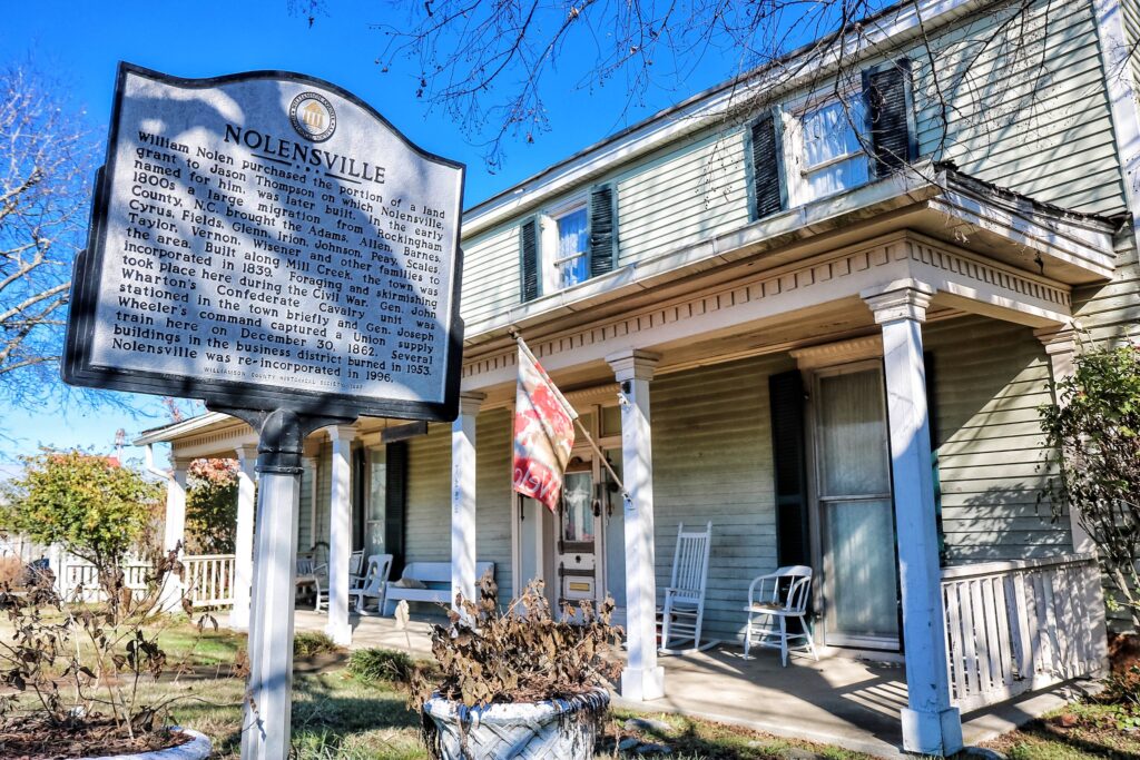 A historic house with a porch and rocking chairs, marked by a sign detailing its history in Williamson County, Tennessee.