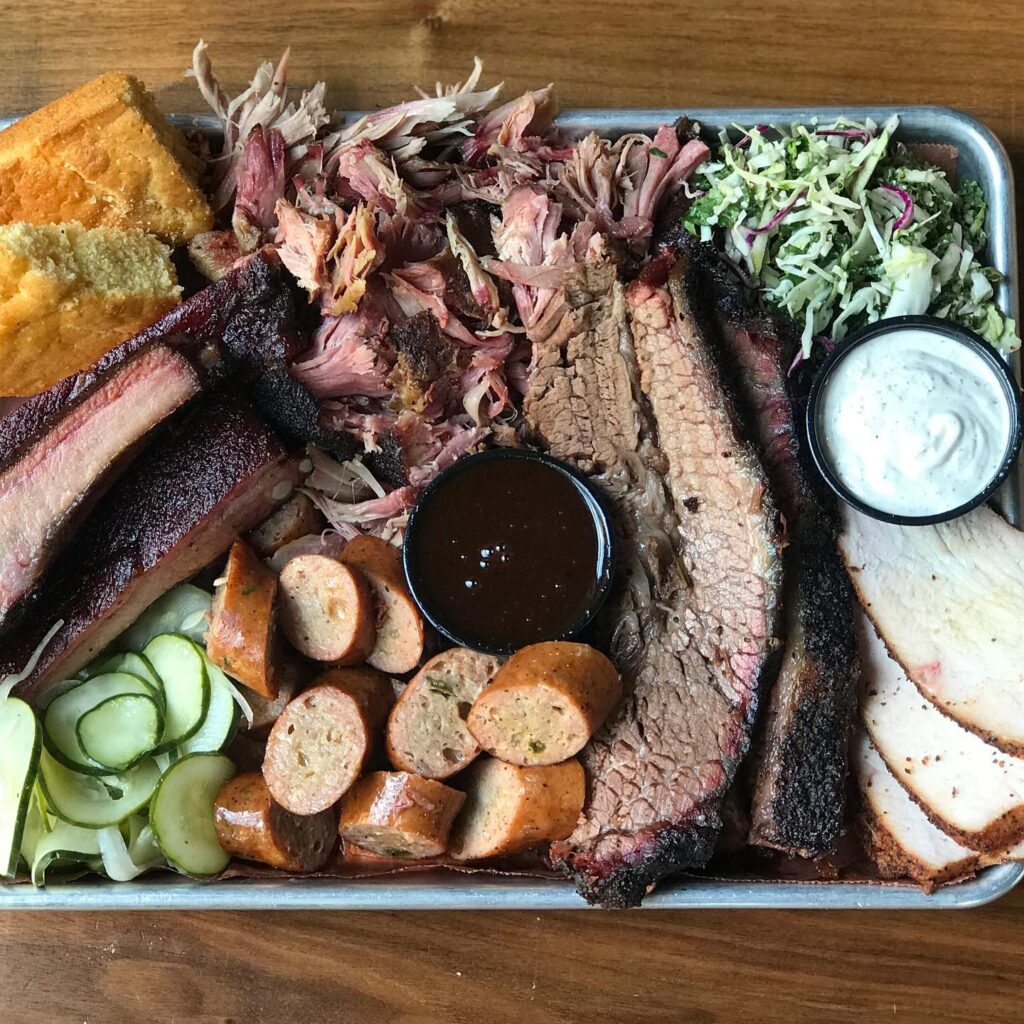 Assorted smoked meats platter with sides of coleslaw, pickles, cornbread, and sauces in Williamson County, Tennessee.