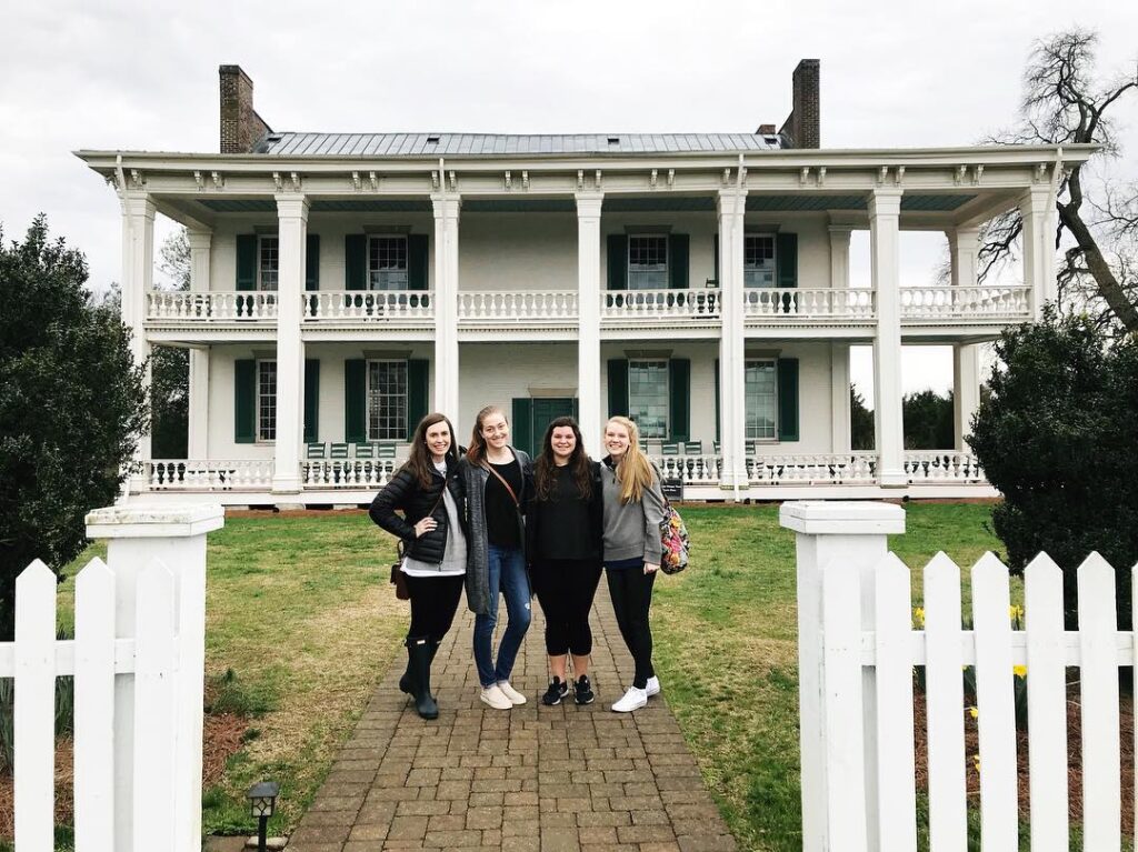 Five women stand on a brick path in front of a large white two-story house with columns in Williamson County, Tennessee.