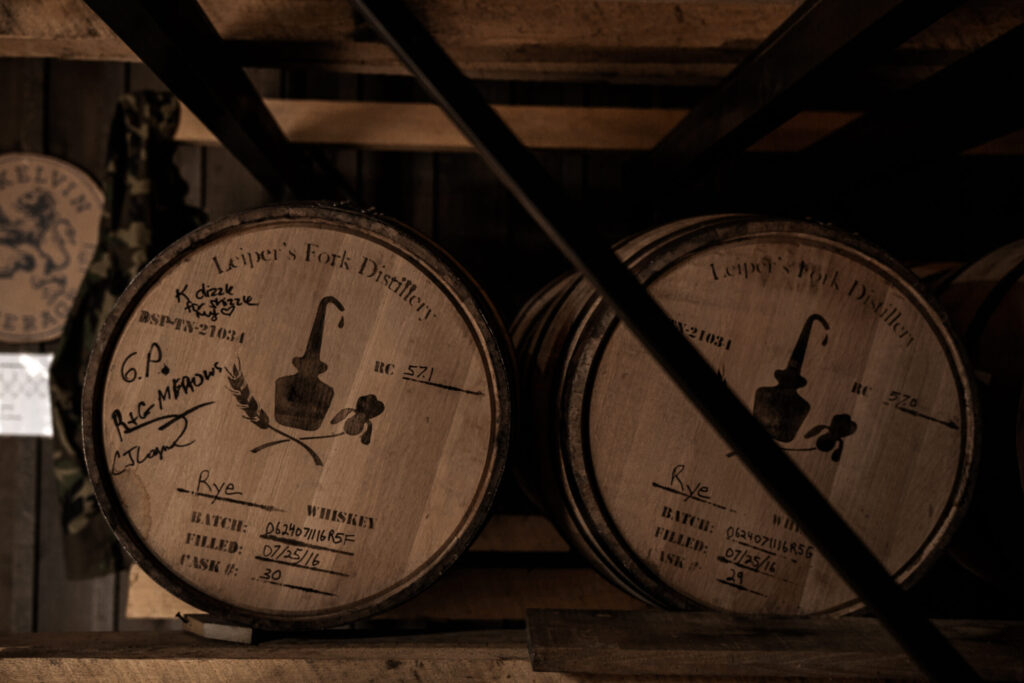 Two wooden whiskey barrels with labels and markings sit on a rack in a dimly lit warehouse in Williamson County, Tennessee.