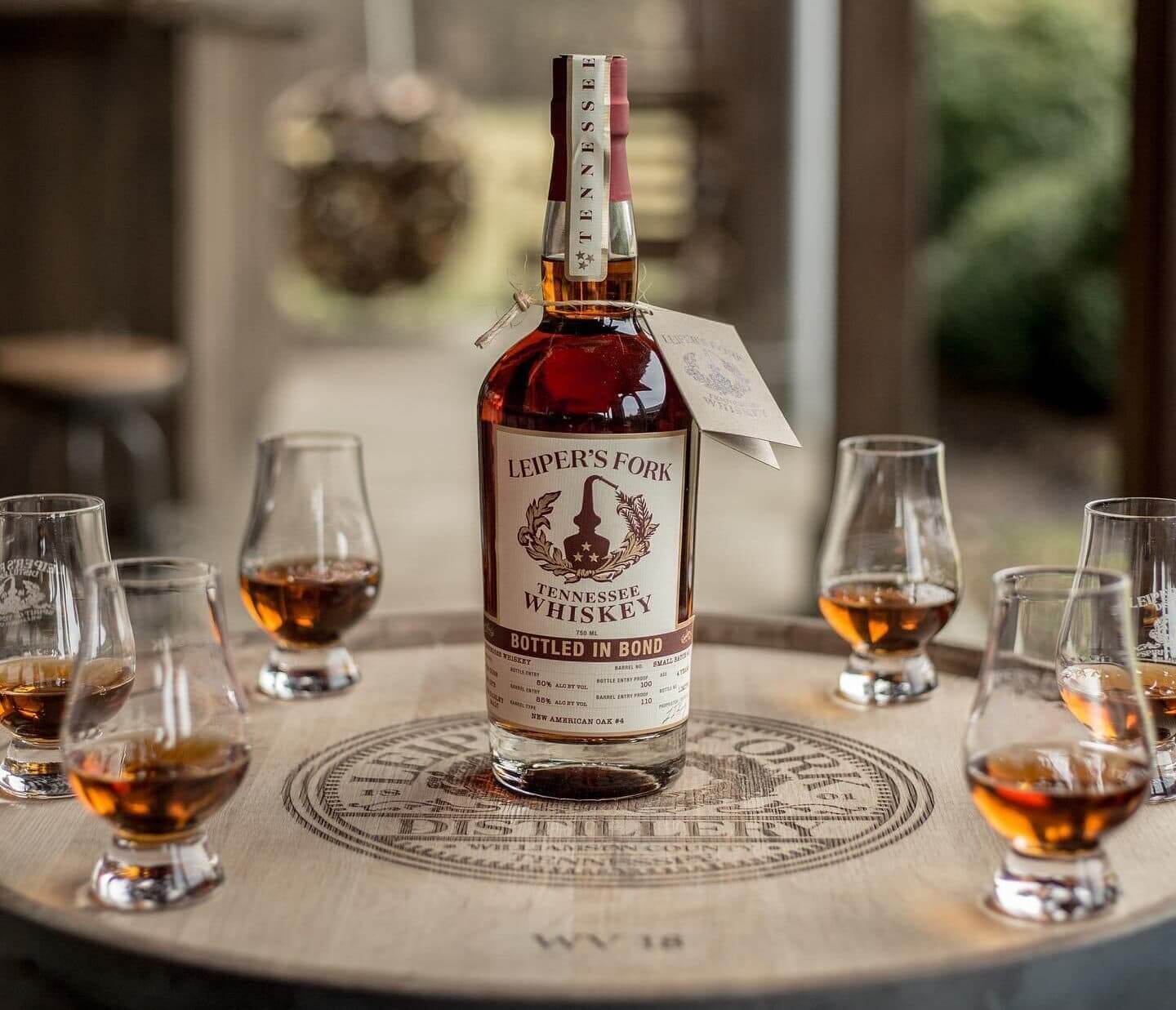 Leiper's Fork Distillery A bottle of Leiper's Fork Tennessee whiskey sits on a wooden barrel surrounded by small glasses filled with amber liquid in Williamson County, Tennessee.