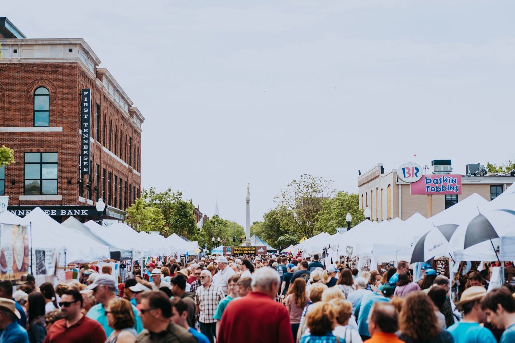 Main Street Festival A bustling outdoor market with white tents lines a city street, filled with shoppers and vendors under a clear blue sky in Williamson County, Tennessee.