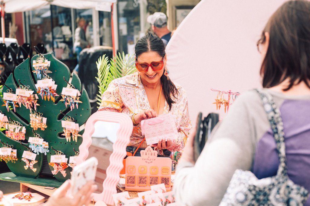 Main Street Festival A woman in a colorful blouse and sunglasses is selling handmade jewelry at an outdoor market, surrounded by vibrant earrings and accessories in Williamson County, Tennessee.