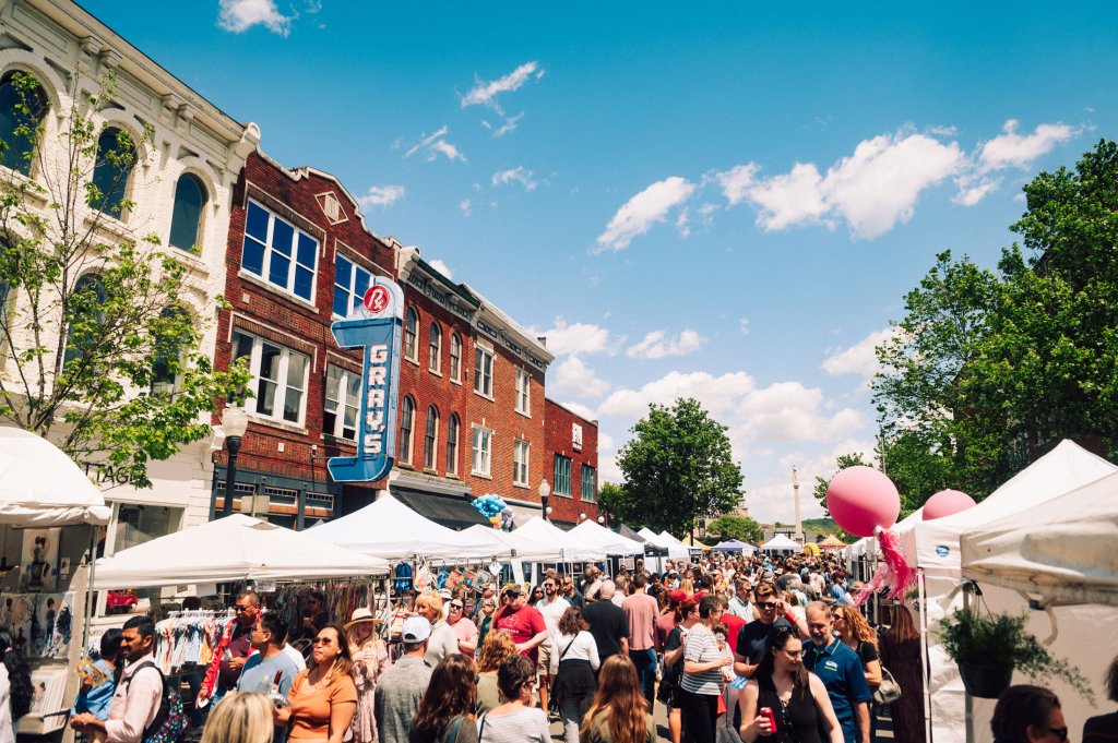 Main Street Festival A bustling outdoor market fills a town square with white tents, shoppers, and colorful balloons against a backdrop of historic brick buildings and a clear blue sky in Williamson County, Tennessee.