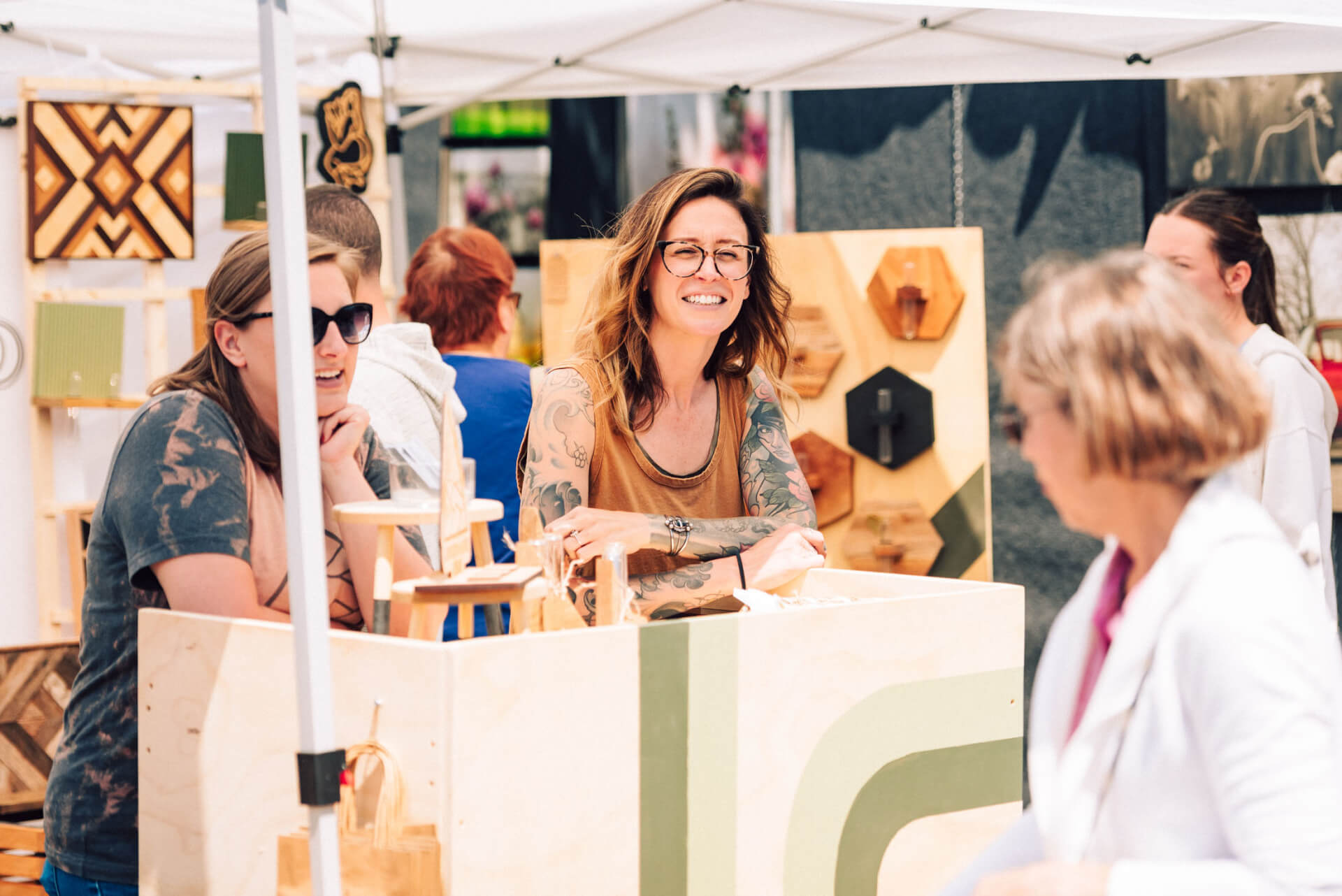 Main Street Festival A group of women are gathered around a wooden booth at an outdoor market, browsing and chatting about the handcrafted items on display in Williamson County, Tennessee.