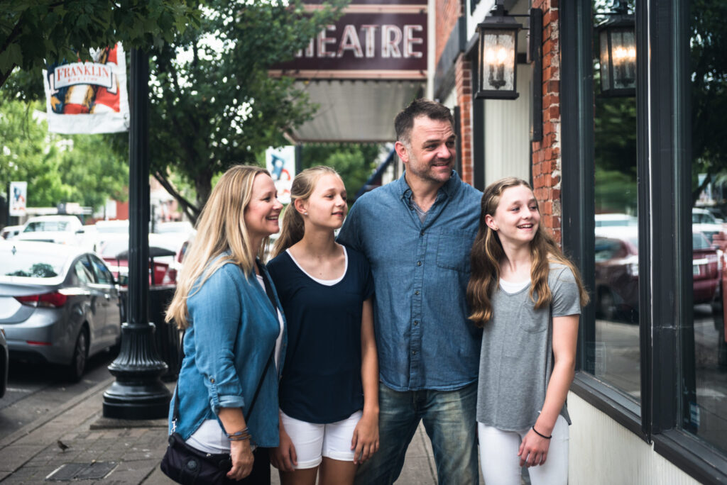 The Best Places in Franklin To Explore With Teens in Tow A family of four, including two girls and a boy, are walking down a street lined with shops and cars in Williamson County, Tennessee.