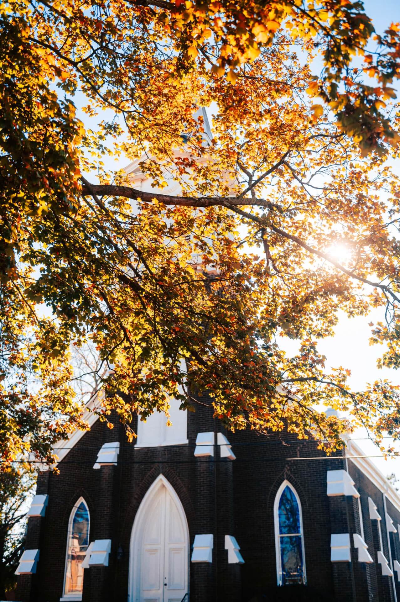 A dark brick church with a white door and stained glass window is framed by autumn leaves in Williamson County, Tennessee.