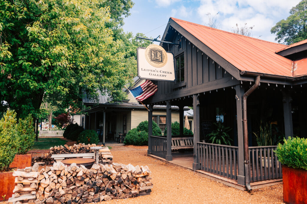 A rustic gallery with a red roof and porch, surrounded by greenery and a woodpile in Williamson County, Tennessee.