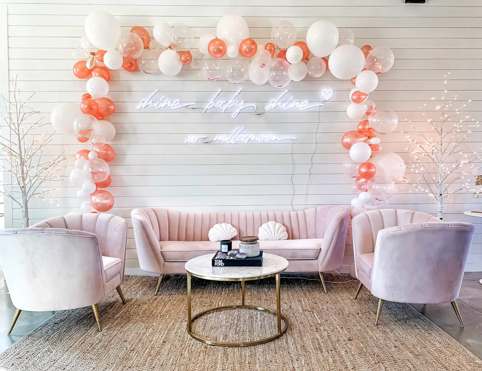 A pastel pink living room with a gold coffee table, balloon arch, and neon sign in Williamson County, Tennessee.