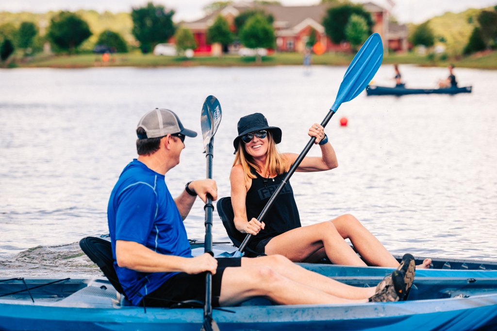 A couple enjoys a leisurely kayak ride on a calm lake, surrounded by lush greenery and distant houses in Williamson County, Tennessee.