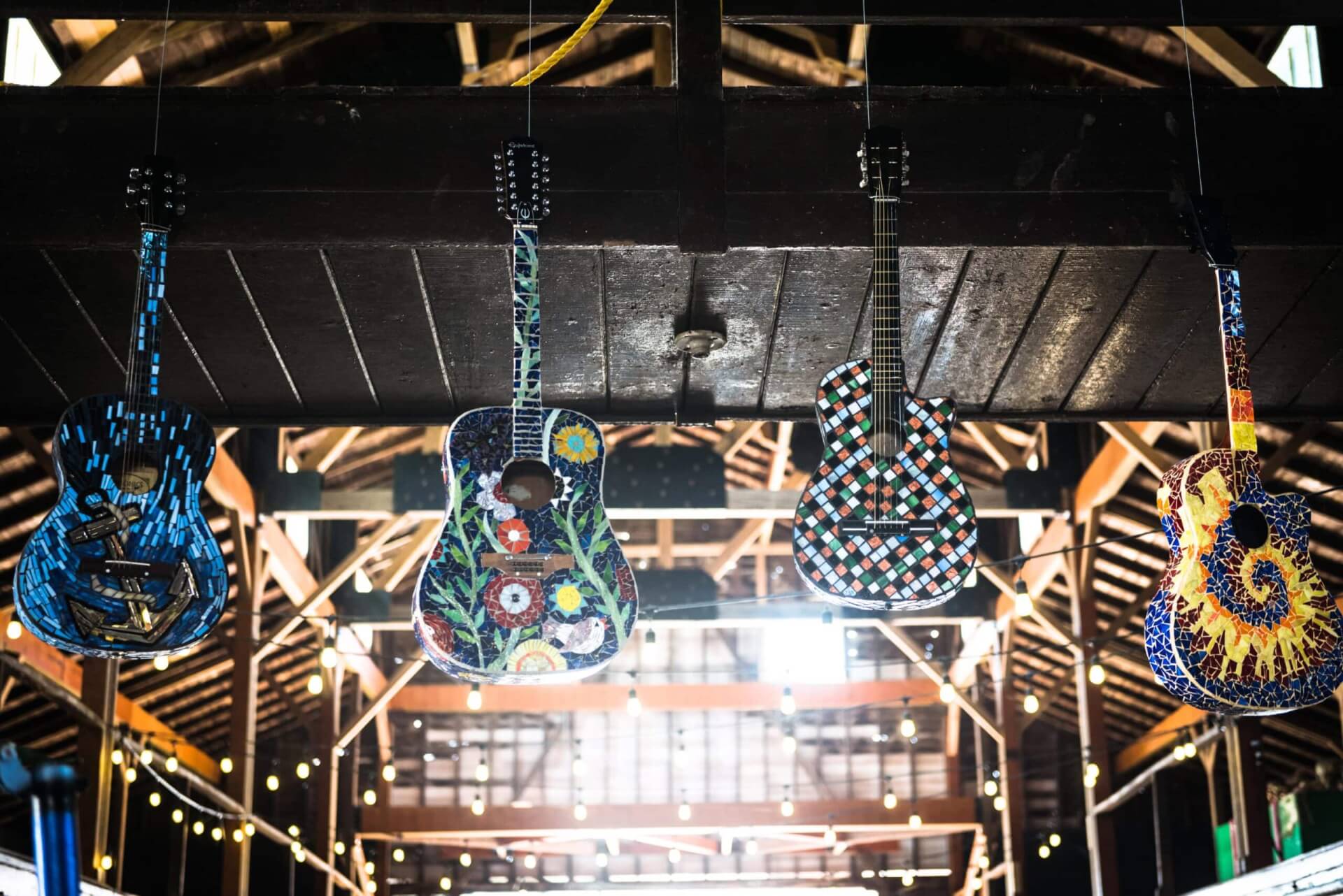 Colorful, painted acoustic guitars hanging from barn ceiling