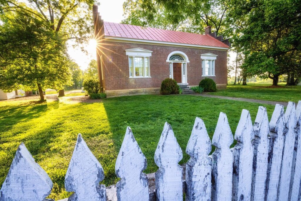 A quaint brick house with a red roof is nestled among lush green trees and a white picket fence in Williamson County, Tennessee.