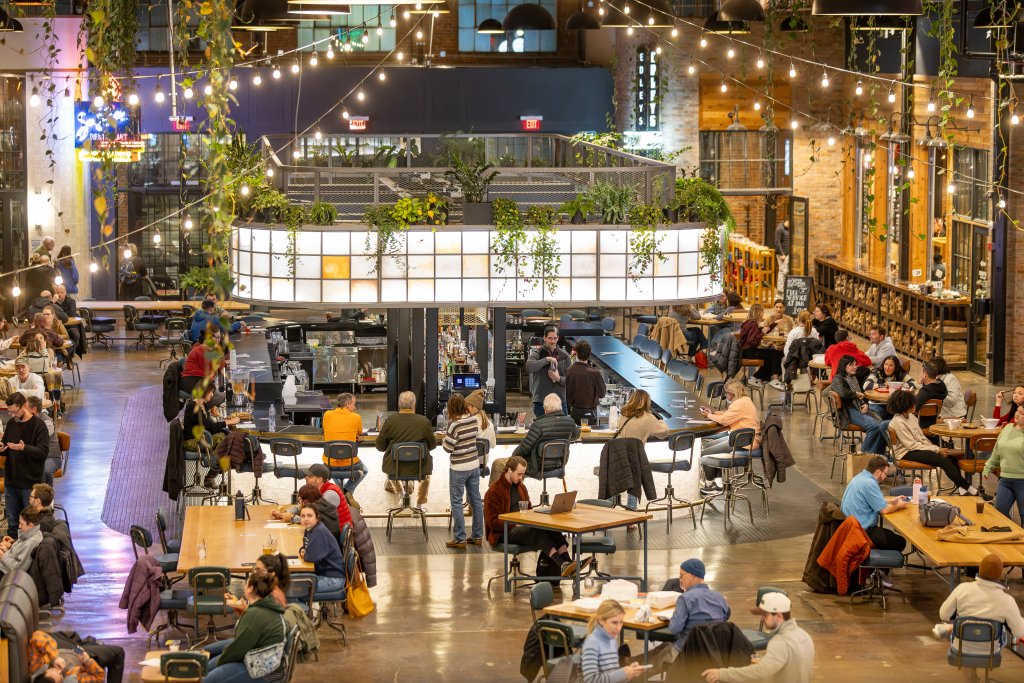 A bustling indoor food hall with hanging plants, string lights, and people dining at tables in Williamson County, Tennessee.