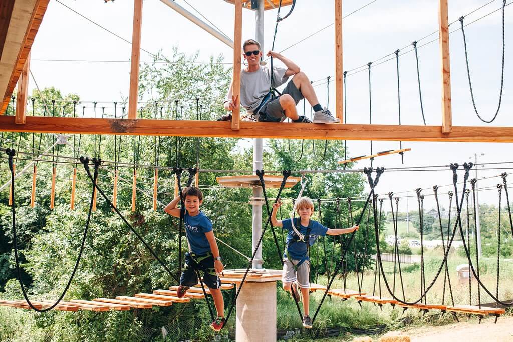 Discover 12 Fun Things To Do With Young Kids in Franklin, TN Three children and an adult are enjoying an aerial ropes course, with the children suspended on ropes and the adult sitting on a wooden platform above in Williamson County, Tennessee.