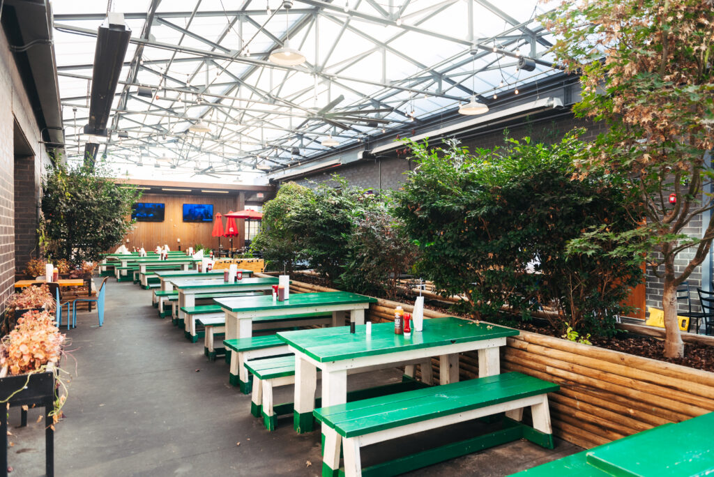 Celebrate Patio Season at Some of Franklin's Best Outdoor Dining Experiences Outdoor dining area with green picnic tables, potted plants, and a glass roof in Williamson County, Tennessee.